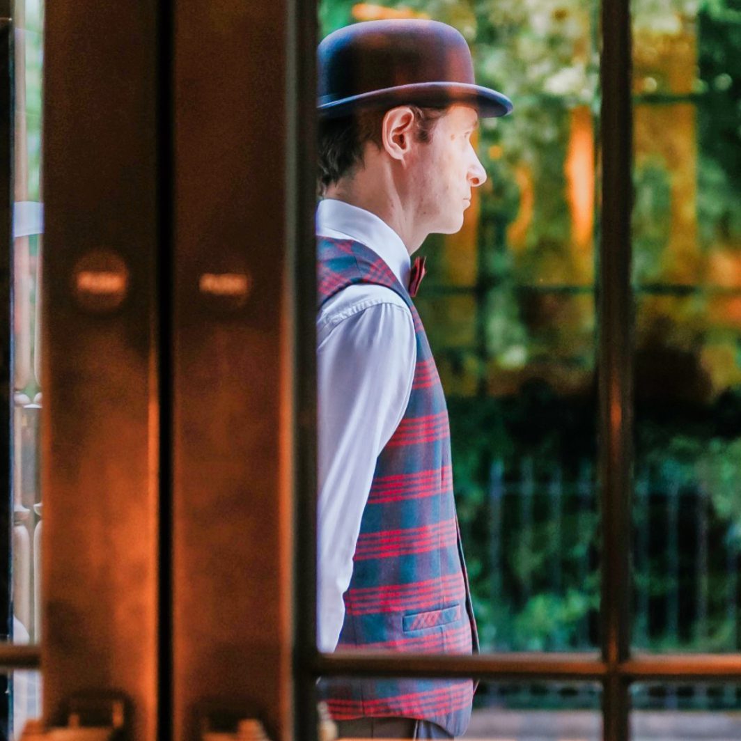 doorman wearing red tartan waistcoat and hotel uniform